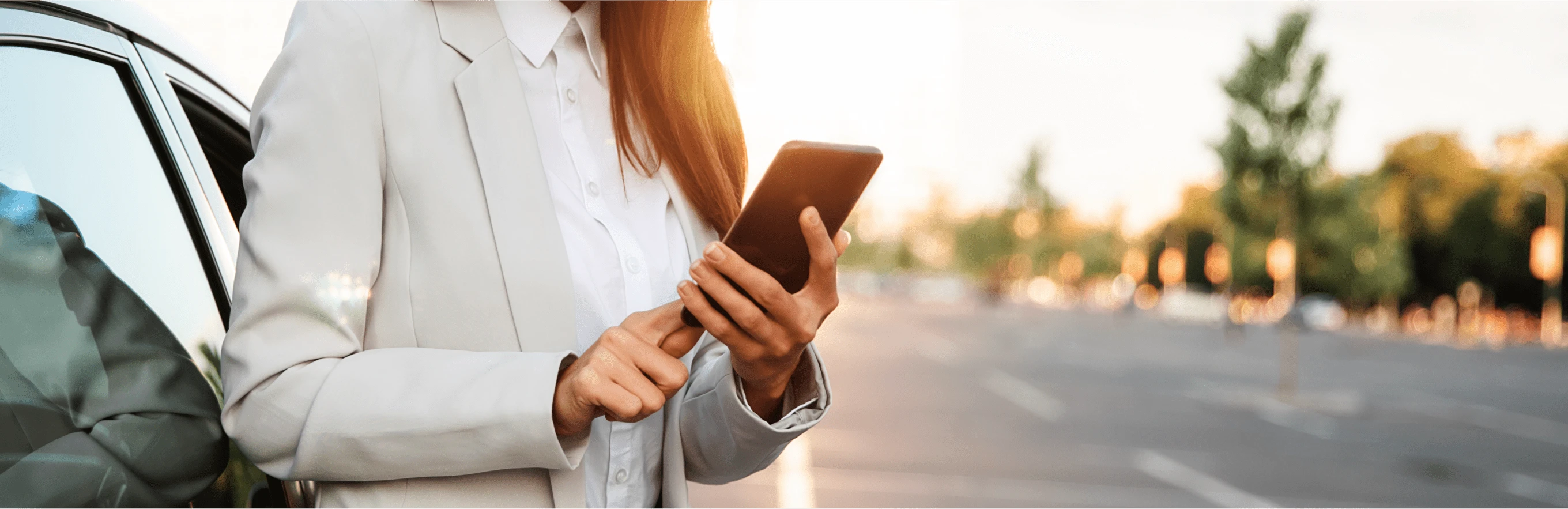 Une femme s'appuie sur sa voiture et tape sur son smartphone pour trouver des magasins et des services locaux avec des réductions à proximité.